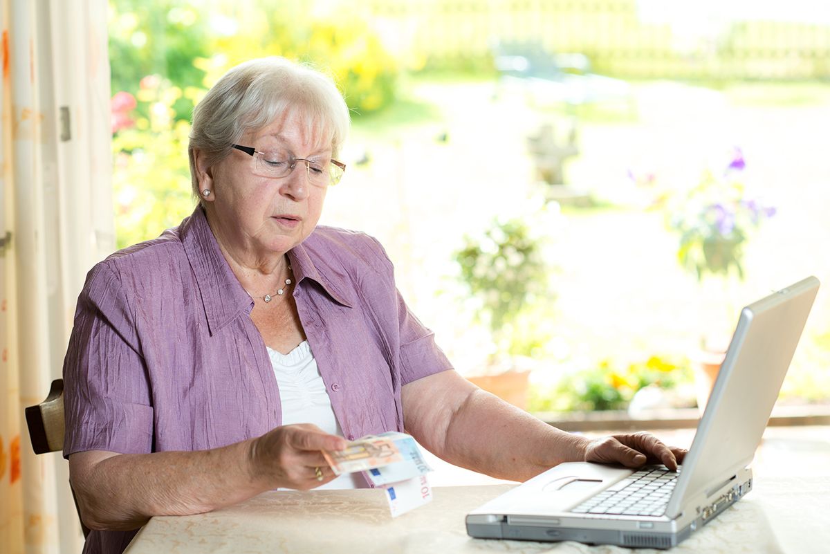Female,Senior,With,Money,In,Hand,Using,Computer,At,Home