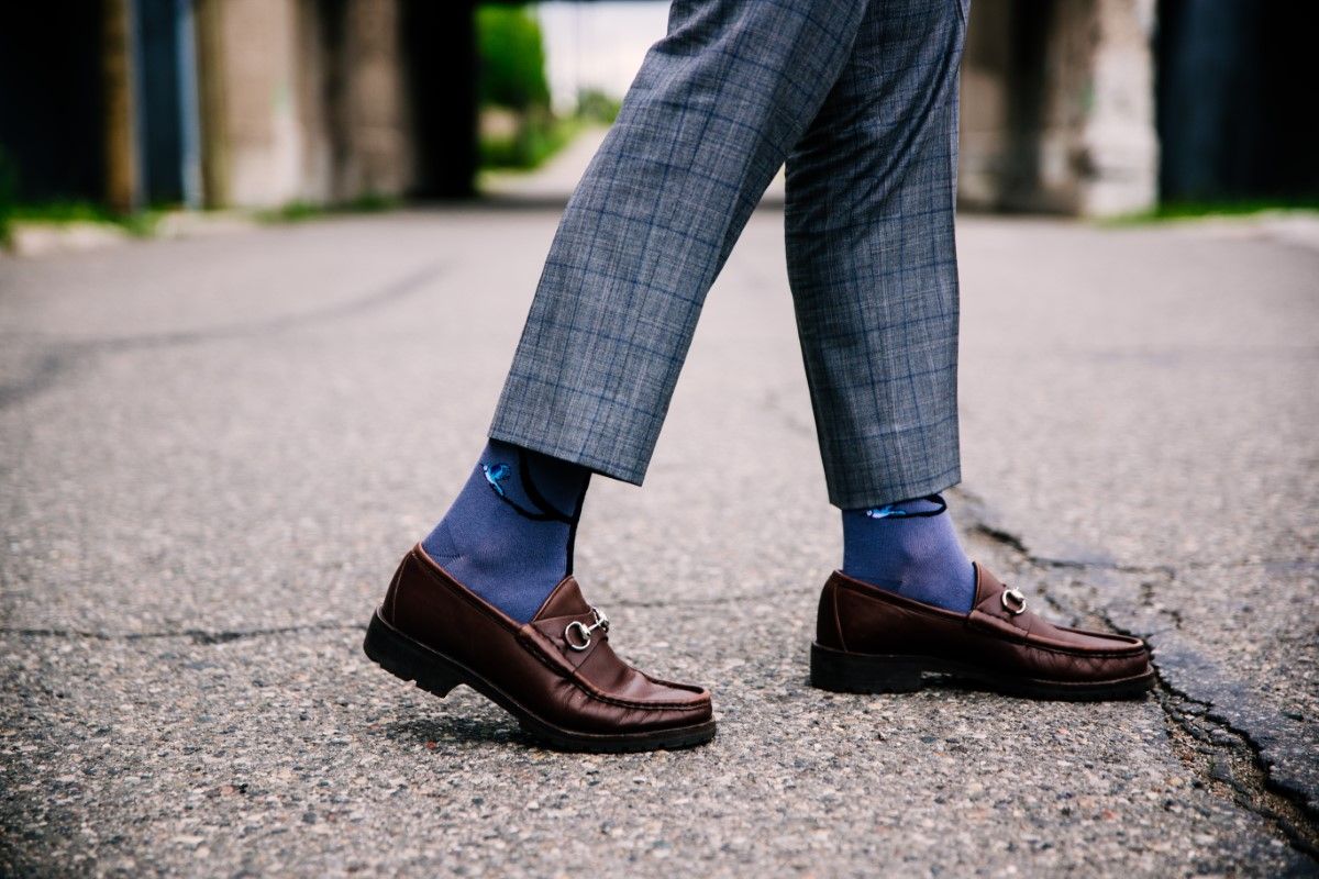 Selective closeup shot of a person wearing blue pants and brown shoes with blue socks
