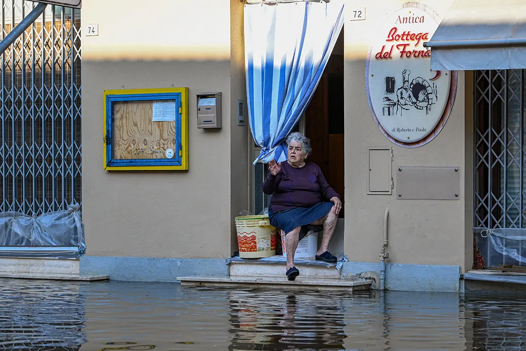 A resident sits on the doorstep of a bakery in a flooded street on May 21, 2023 in Conselice, near Ravenna, after deadly floodwaters hit the Emilia-Romagna region. More than 36,000 people have now been forced from their homes by deadly floods in northeast Italy, regional officials said, as rising waters swallowed more houses and fresh landslides isolated hamlets. Violent downpours earlier this week killed 14 people, transforming streets in the cities and towns of the Emilia Romagna region into rivers. (Photo by Andreas SOLARO / AFP)