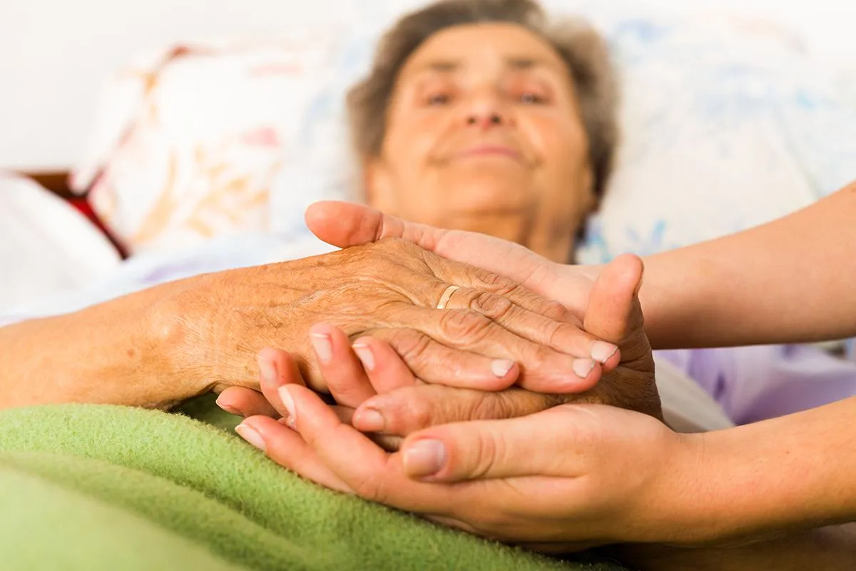 Caring,Nurse,Holding,Kind,Elderly,Lady's,Hands,In,Bed.