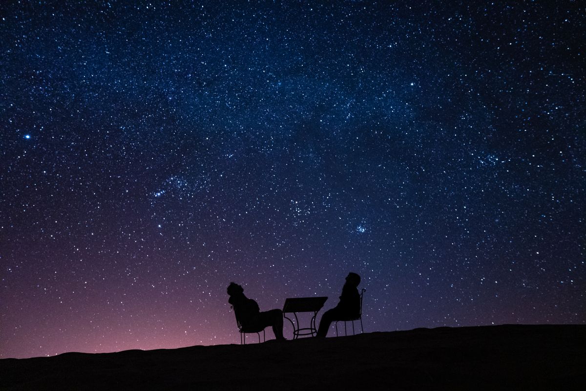 Young,Couple,Sitting,At,A,Table,On,A,Desert,Dune