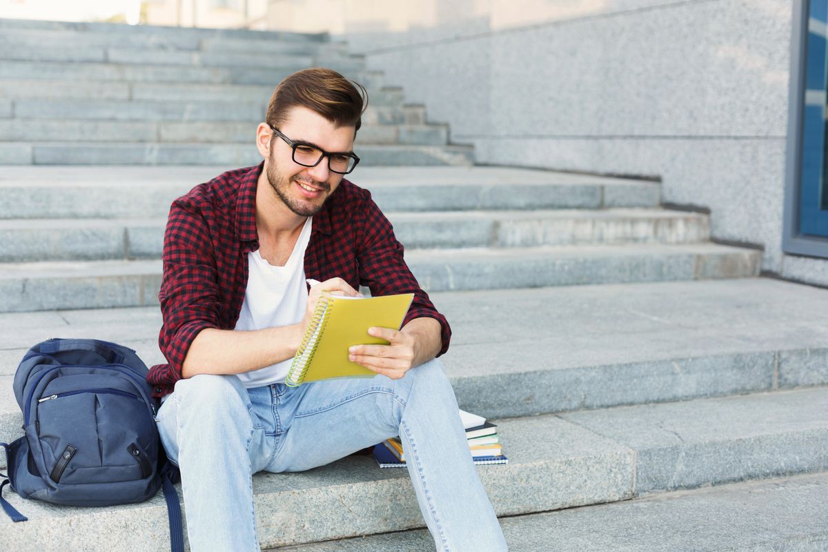 Young student making notes sitting on stairs