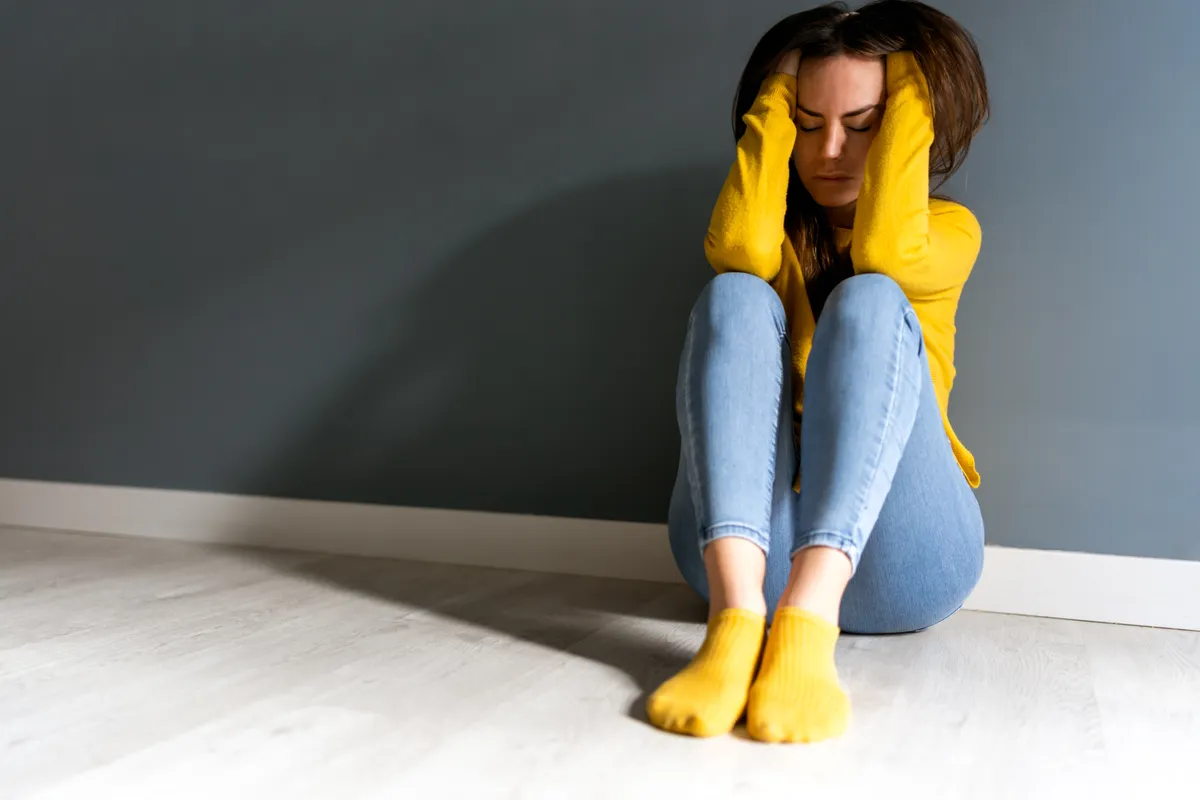 Upset young woman with closed eyes touching head near wall