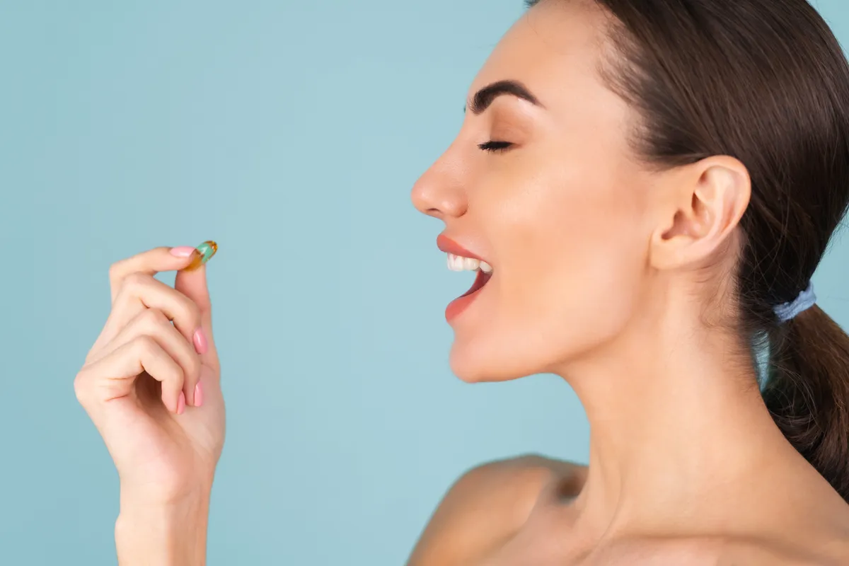 Close-up beauty portrait of a topless woman with perfect skin and natural make-up, holding a supplement, vitamin omega 3, fish oil, on a turquoise background