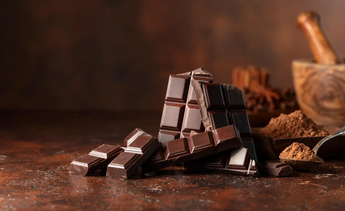 Broken,Dark,Chocolate,Bar,And,Cocoa,Powder,On,A,Brown