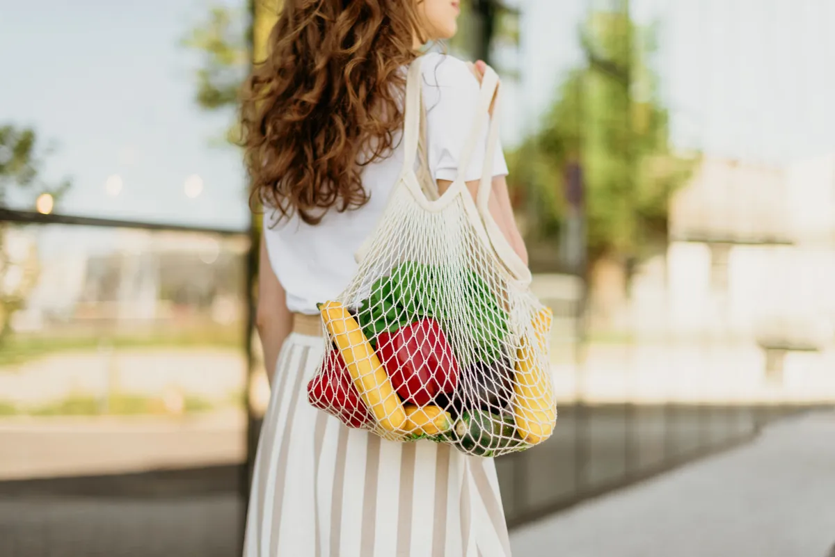 Zero waste concept with copy space. Woman holding cotton shopper and reusable mesh shopping bags with vegetables, products. Eco friendly mesh shopper. Zero waste, plastic free concept.