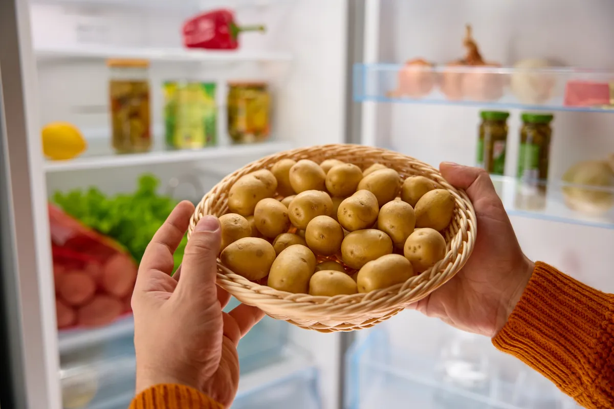Egy kosár krumpli egy férfi kezében egy nyitott hűtőszekrény előtt