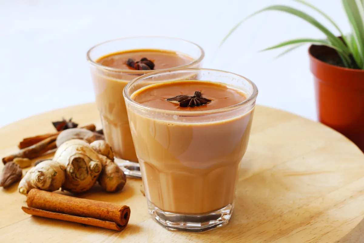 Chai fűszeres tea asztalon, mellette fahéjjal és gyömbérrel