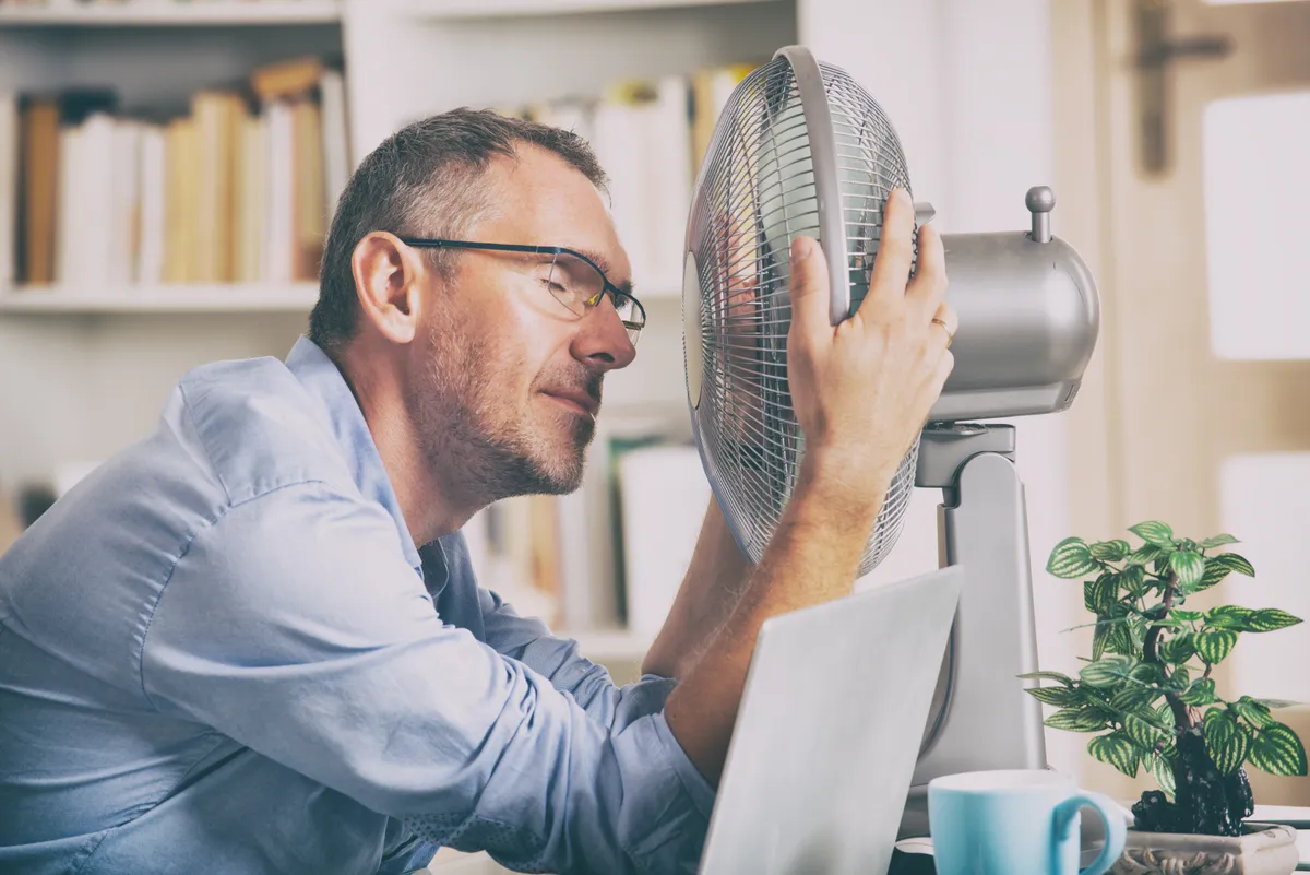 Hőhullám miatt ventilátort az arcába tartó férfi klimax idején