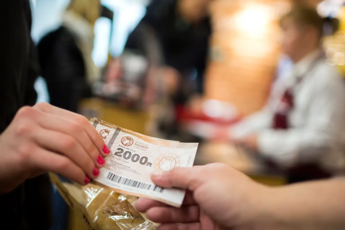 Egy nő nyugdíjas utalvánnyal fizet egy élelmiszerboltban