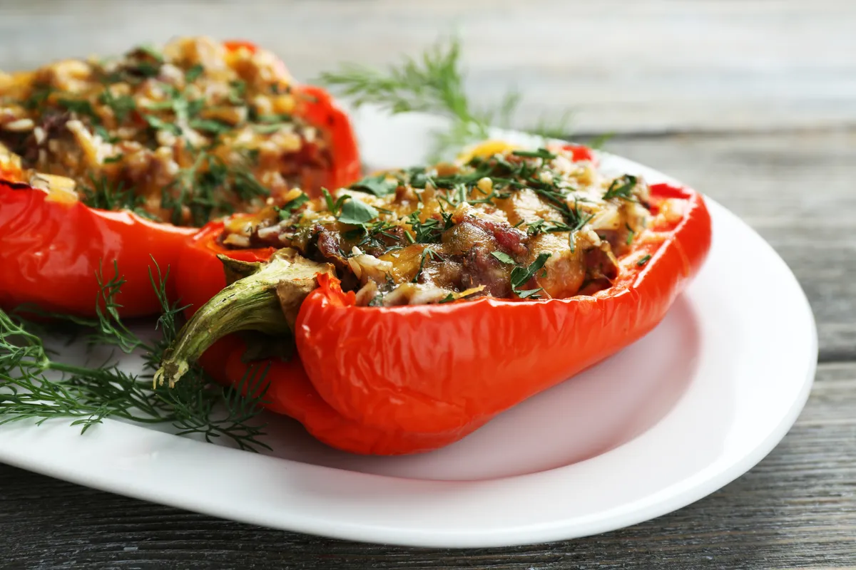 paprikás ételek: töltött paprika fehér tányéron zöldfűszerekkel