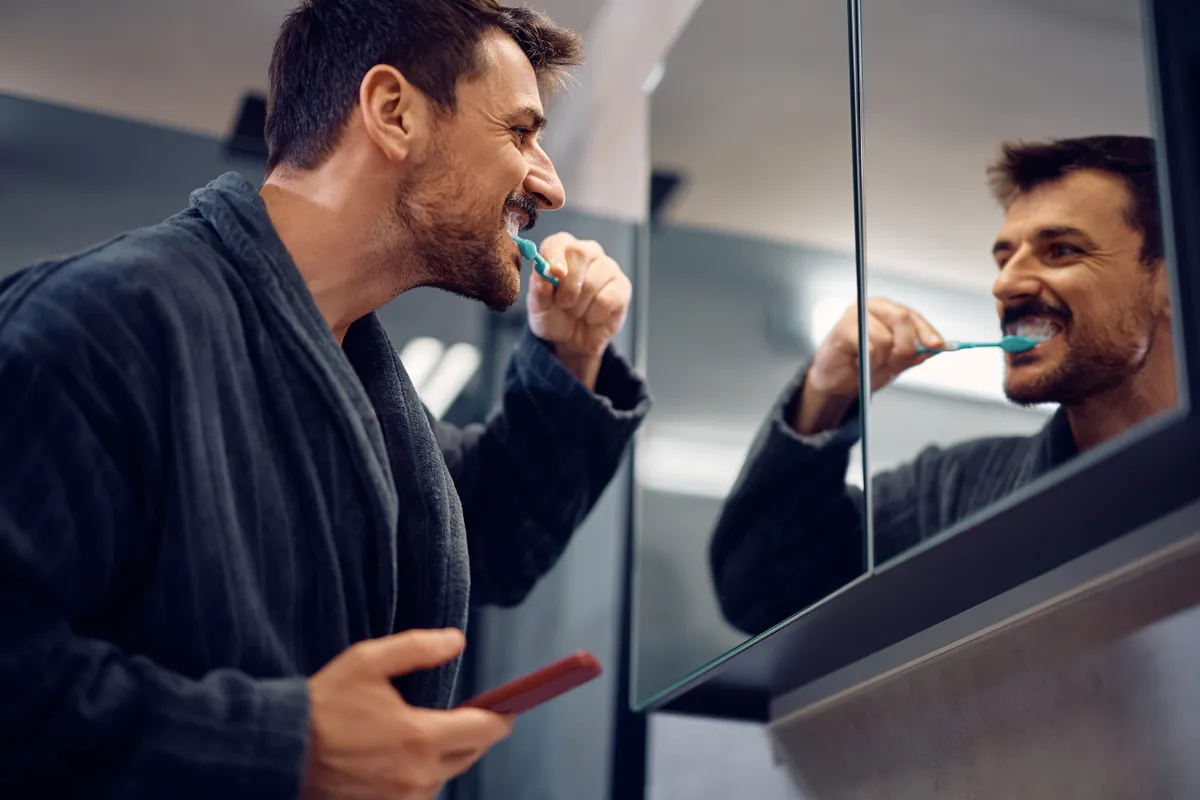 Férfi fogmosás közben a tükör előtt