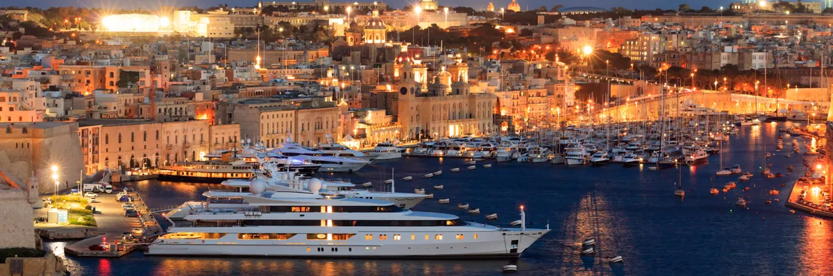 A máltai Valletta kikötőjében horgonyzó luxus jachtok esti kivilágításban