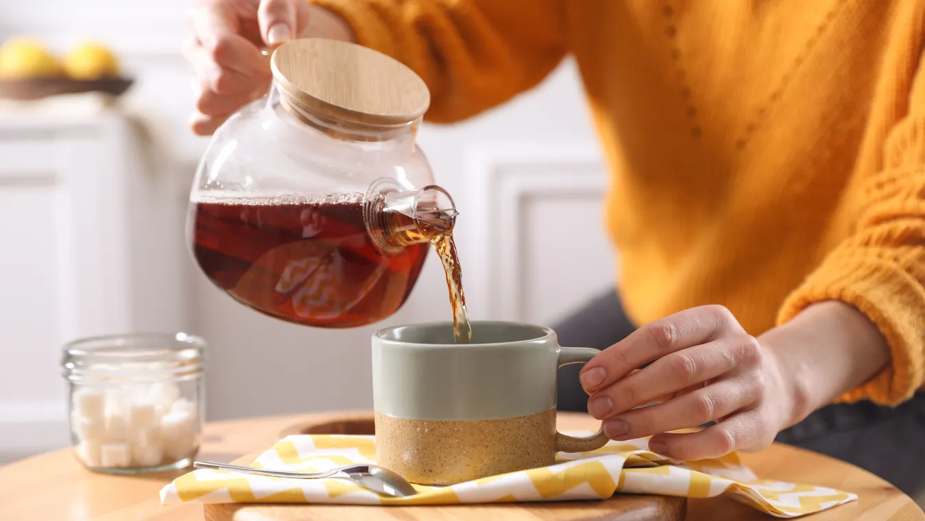 Magas vérnyomásra gyógynövényteát csészébe öntő fiatal nő