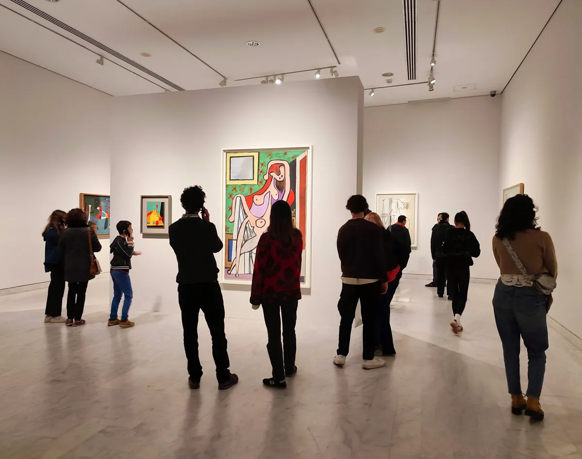 Művészeti galériában festmények előtt kvízt kitöltő közönség