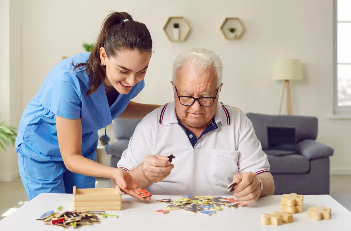 Egy ápolónő segít egy idős, Alzheimer-kórban szenvedő férfinak a memóriajátékban.