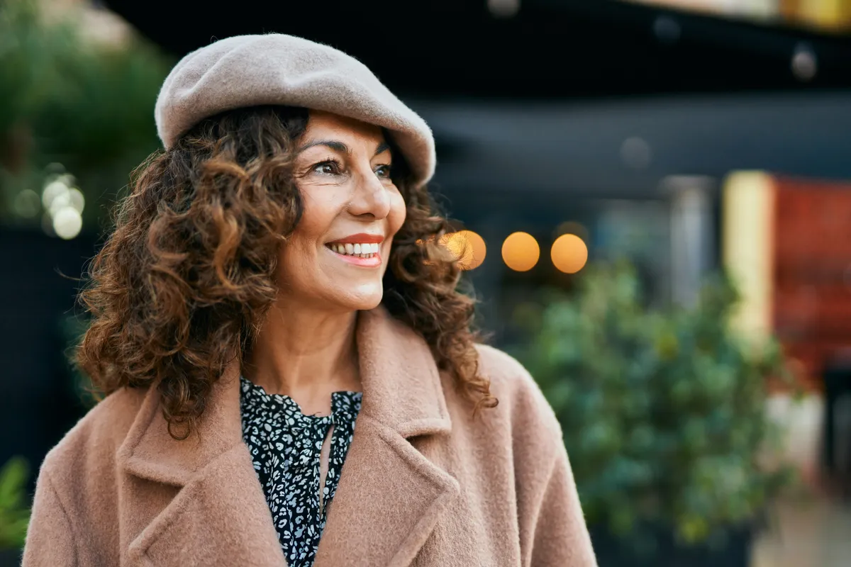 Mosolygó nő bézs kabátban és barett sapkában, a francia nők természetes eleganciáját sugározva.