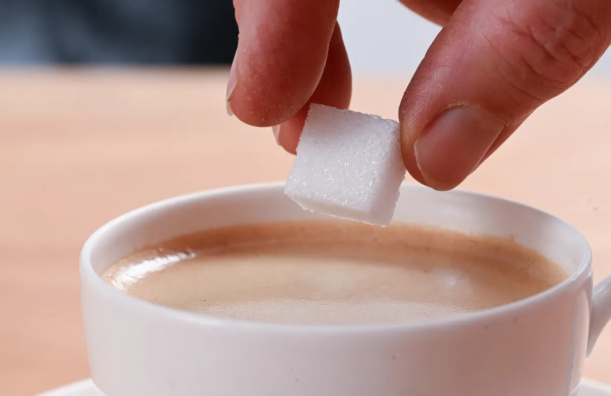 Egy nő kockacukrot tesz egy csésze kávéba