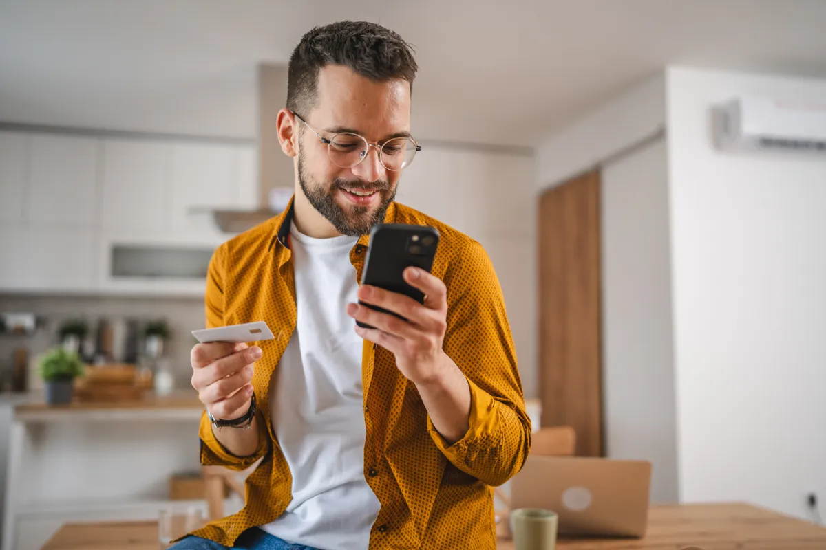 Egy férfi aki ez asztalon ül a telefonját nyomkodja online bankol