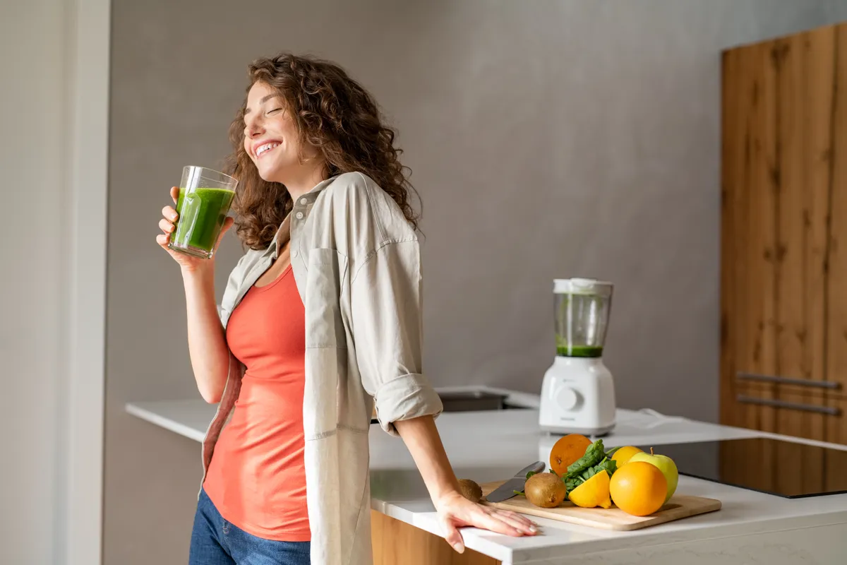 Az immunrendszere működését zöldségek smoothie-val támogató fiatal nő a konyhájában