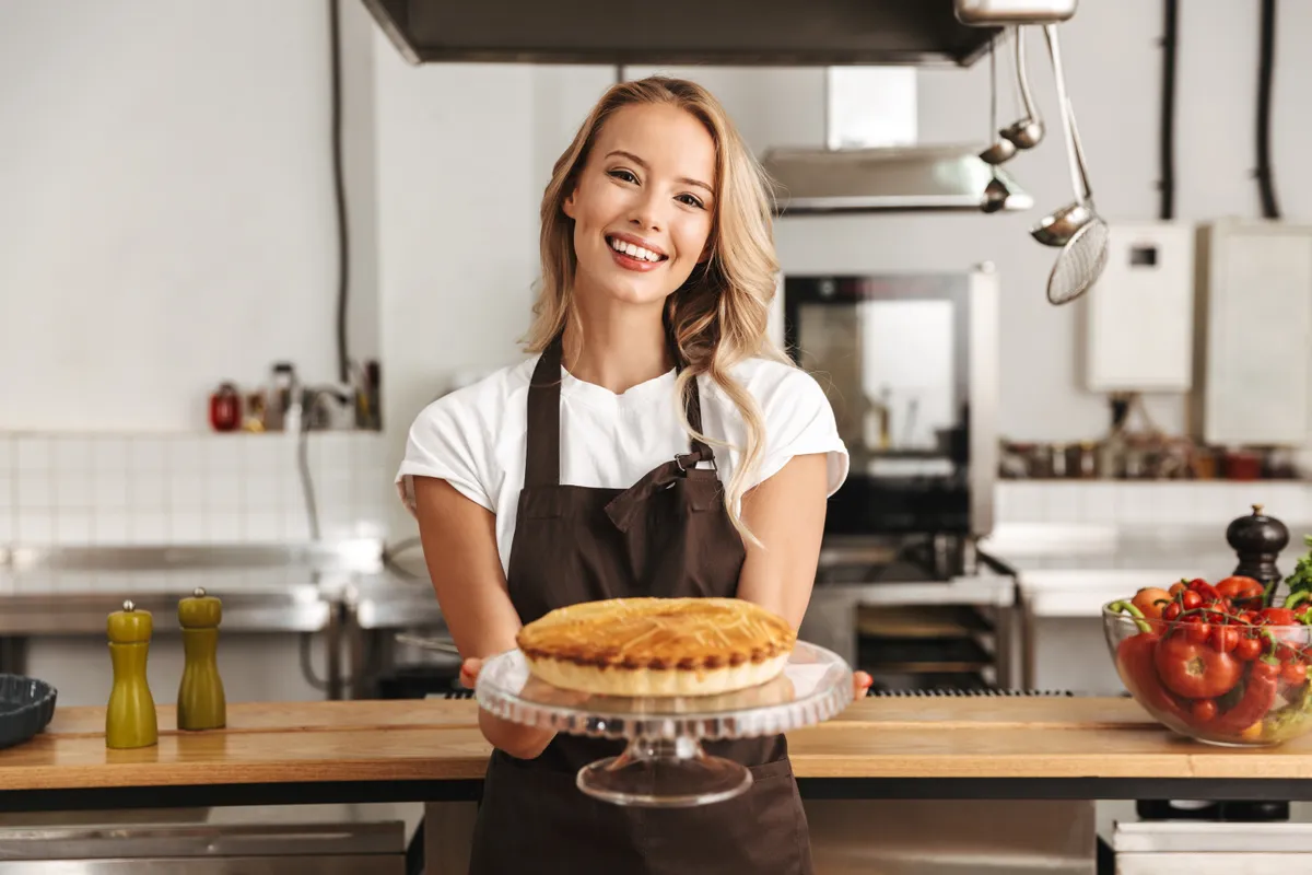 Egy nő egy tál szilvás pitét tart a kezében a konyhában ami az egyik legjobb szilvás receptből készült