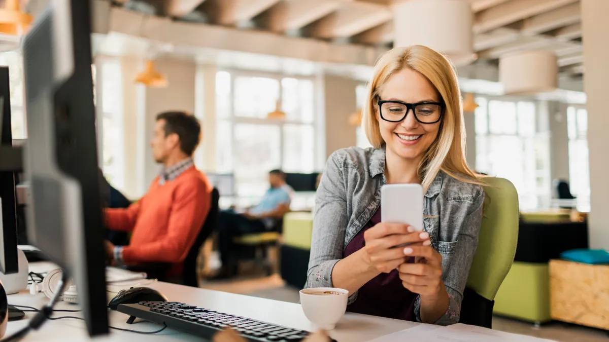 Egy nő az irodában a telefonján tölt ki egy magyar közmondások kvízt 