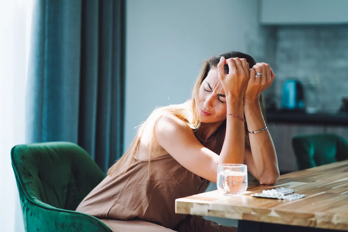 Loneliness and break up aftermath. Crying woman with head in hands drinking pills on the kitchen
