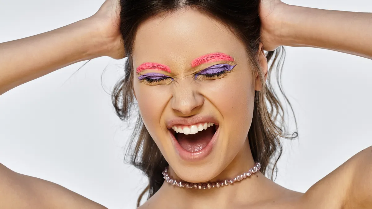 Egy nő extra sminkkel rózsaszín szemöldökkel lila szemhéjfestékkel igazi Ikrek smink.