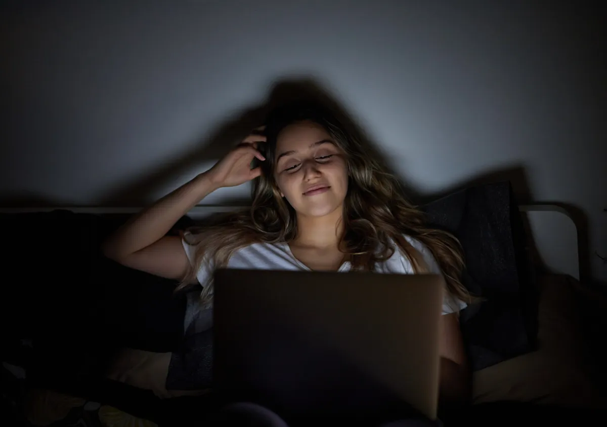 Fiatal nő, aki a laptopján felnőttfilmet néz az ágyában
