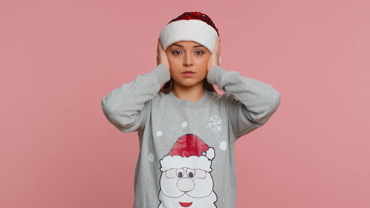 Egy nő aki befogja a fülét mert stresszel a karácsonyi daloktól.