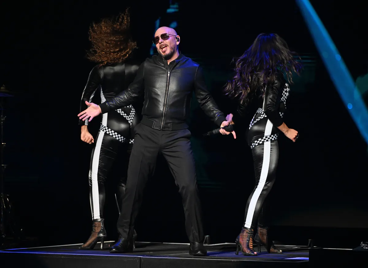 Pitbull fekete bőrdzsekiben háttértáncosokkal énekel.