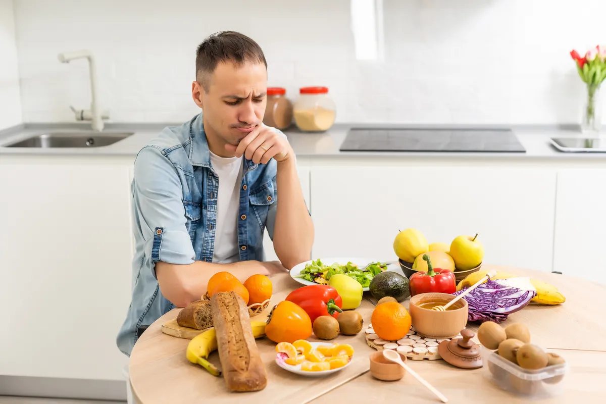 Egy férfi ül egy asztalnál ami tele van zöldségekkel és kenyérfélékkel és azon gondolkodik melyek hatásosak a refluxkezelés során.