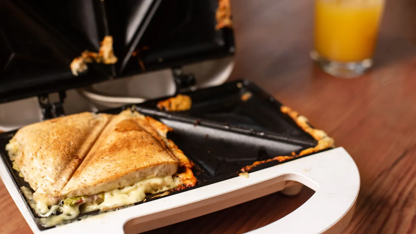 A melegszendvicssütő takarítása sajtos toast készítése után.