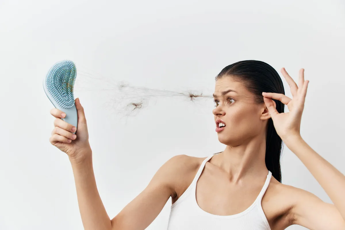 Egy nő fésűjéből a kitépett gubancolódó haját szedi ki elborzadva.