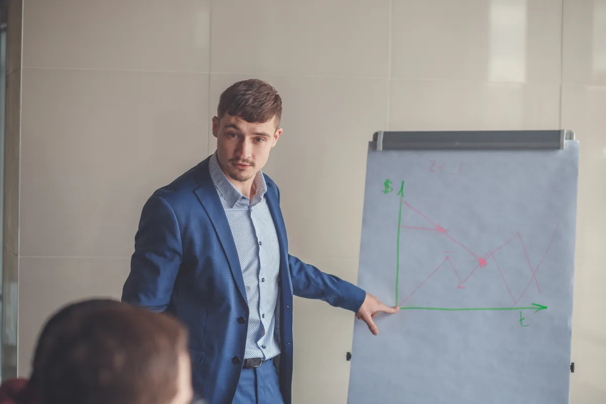 Lottóstratégát magyarázó közgazdász férfi egy tábla előtt.