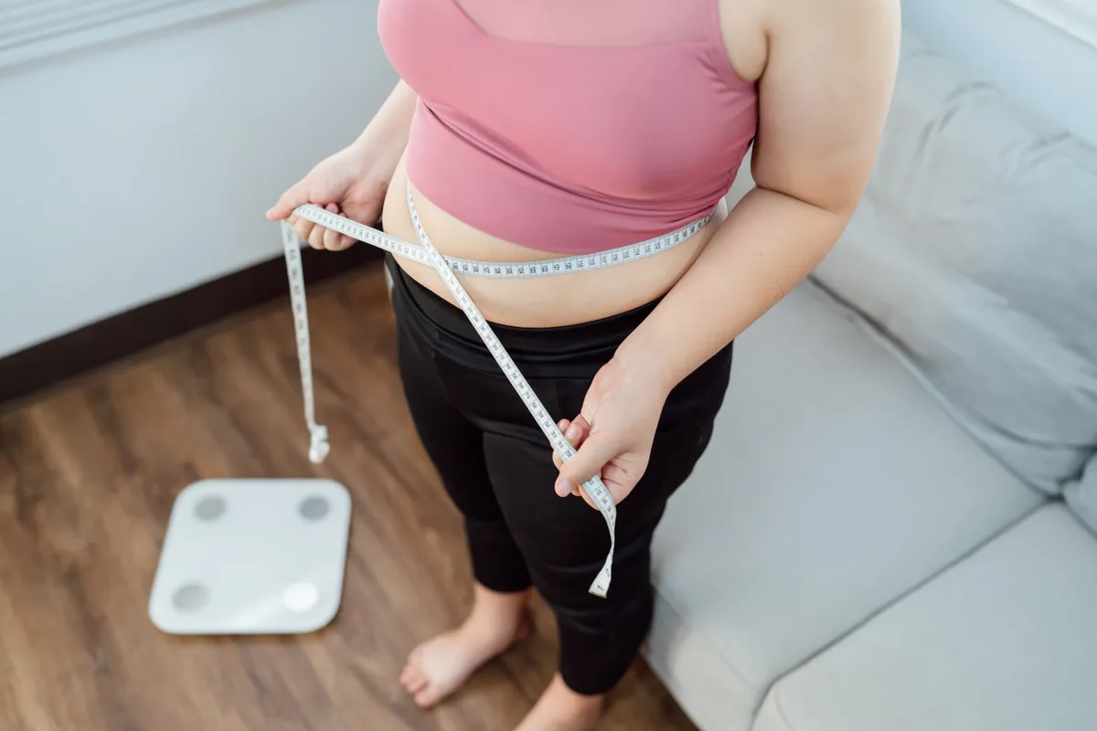Egy nő éppen méri a derekát, aki tartós fogyást ért el.