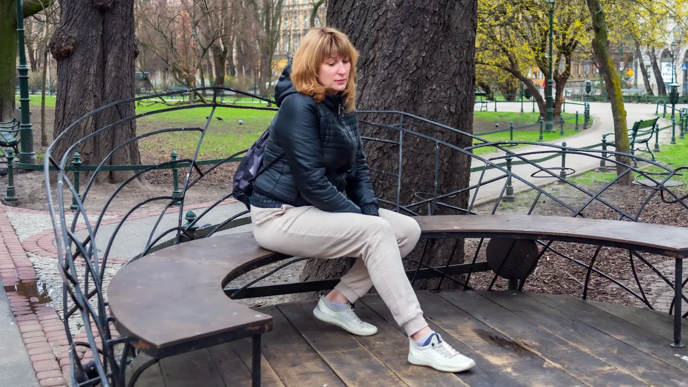 Nő melegítőnadrágban és fekete dzsekiben egy park padján