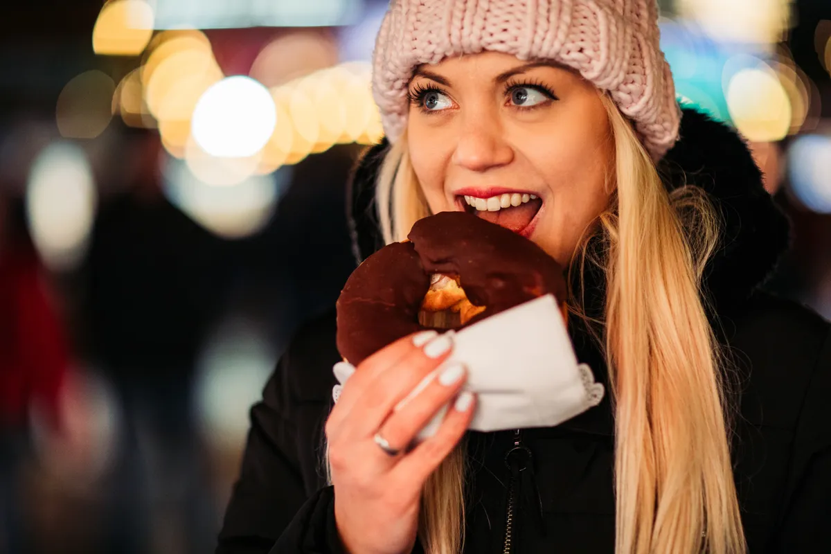 Fogyással küzdő nő, aki éppen finomságot majszol a téli hidegben.