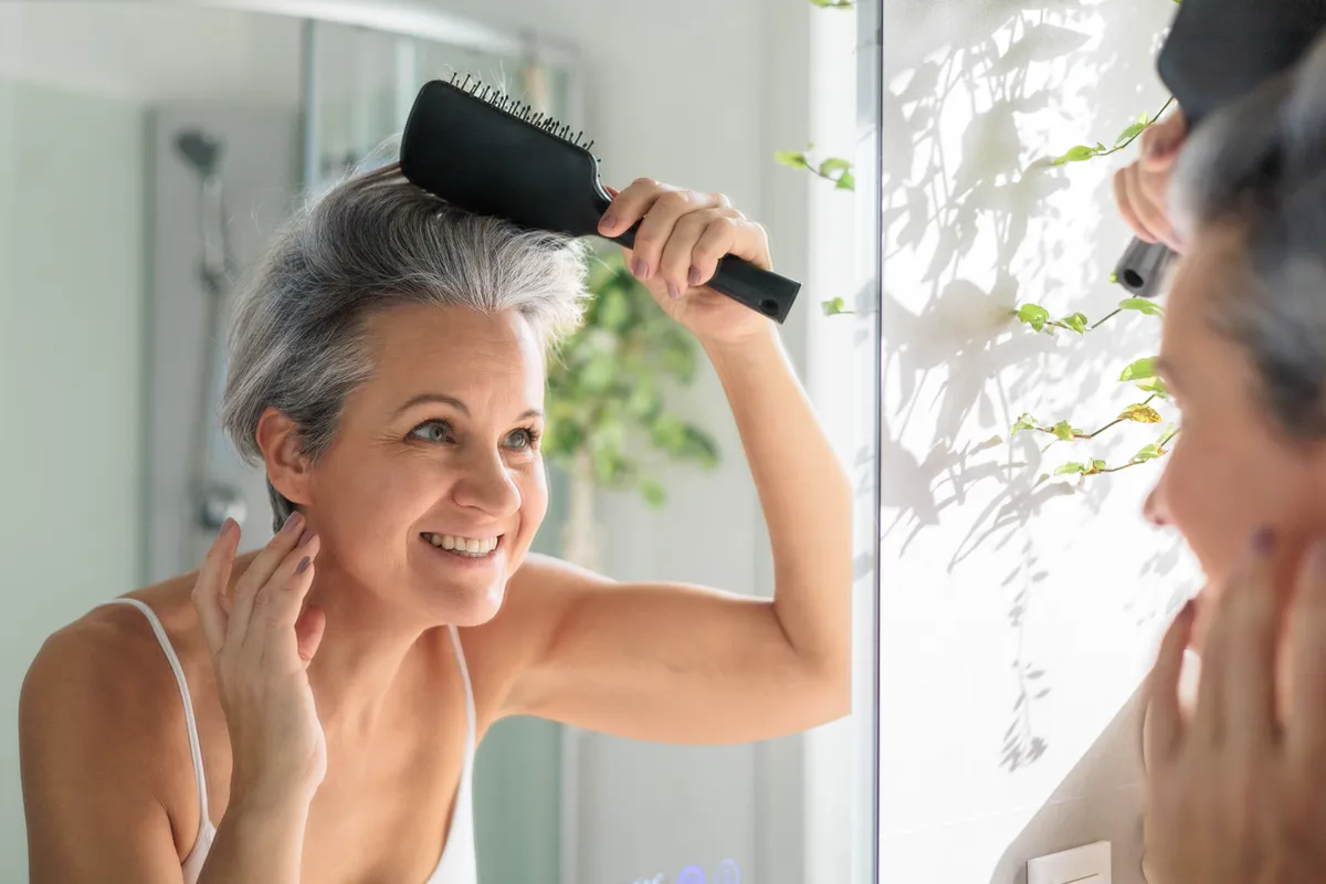 A természetes ősz hajának fésülése közben egy nő a tükörben nézi magát.z.