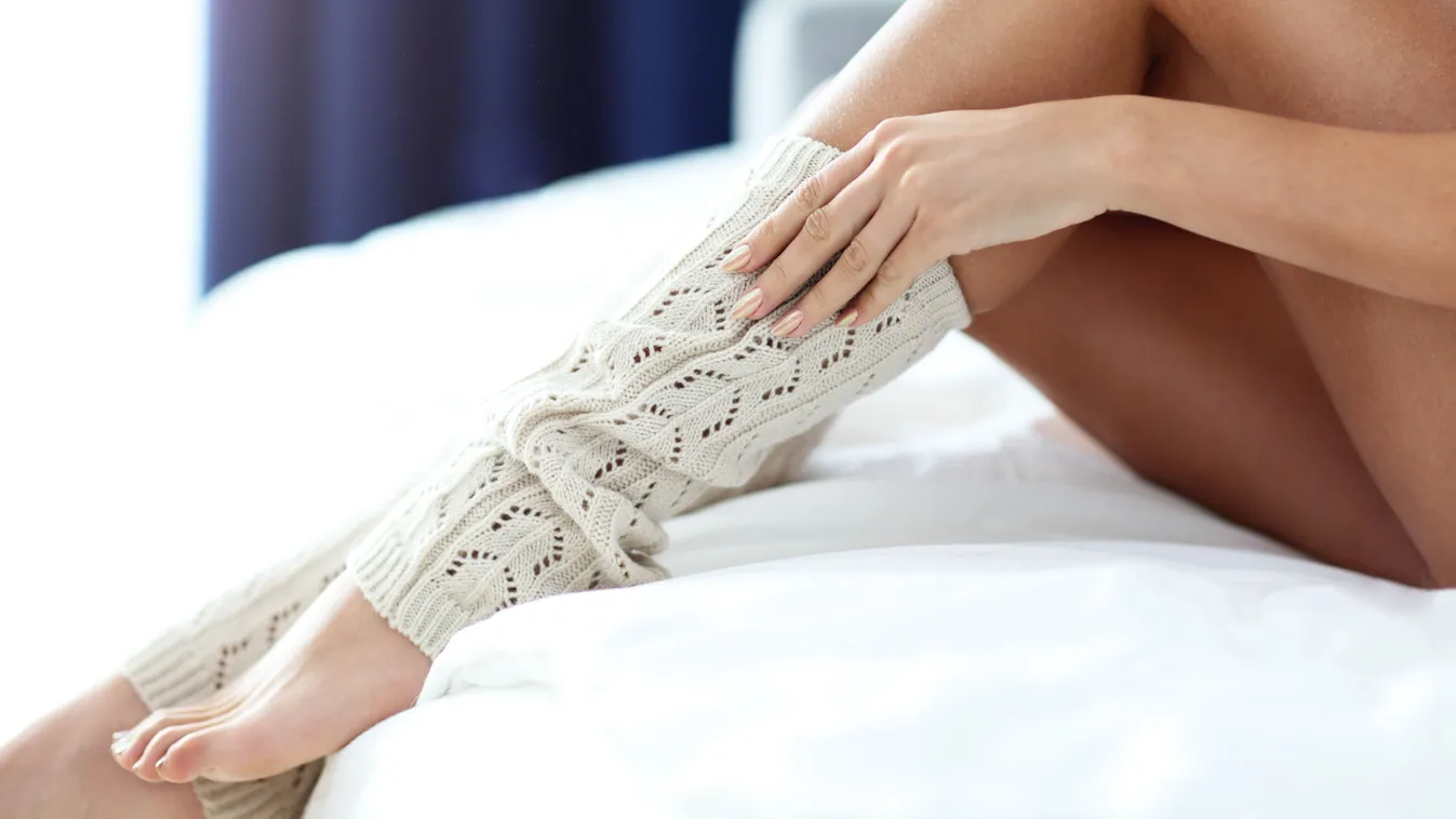 Egy nő ül az ágyon szép, kötött lábszármelegítőben.