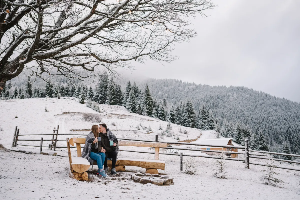 Romantikus téli hétvégék kettesben, a hóval borított tájon csókolózik egy fiatal pár.