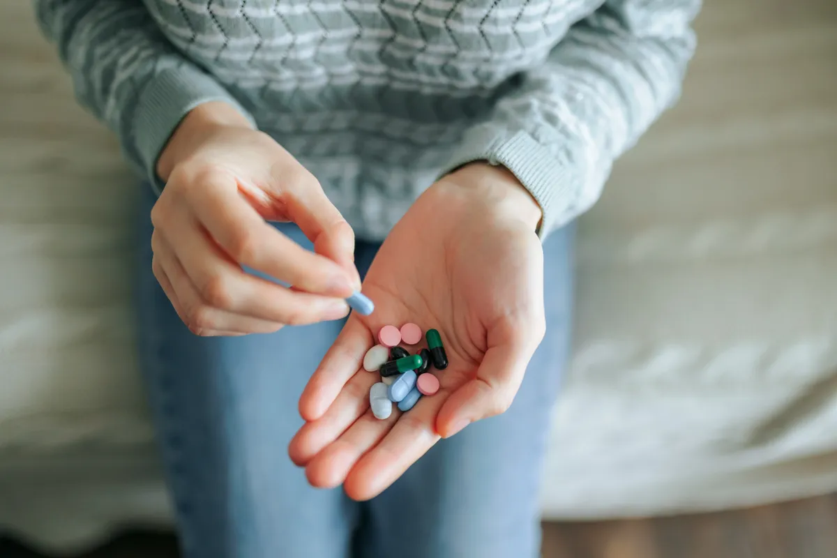 Ülő nő gyógyszereket tart a tenyerében.