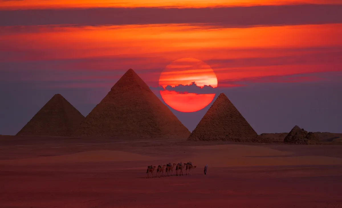 Naplementében elhalad egy tevekaraván a gízai piramisok mellett.