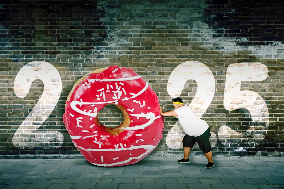 Személyiségteszt az újévi fogadalmakról: túlsúlyos férfi görget maga előtt egy hatalmas fánkot, a héttérben a 2025 felirat látható.