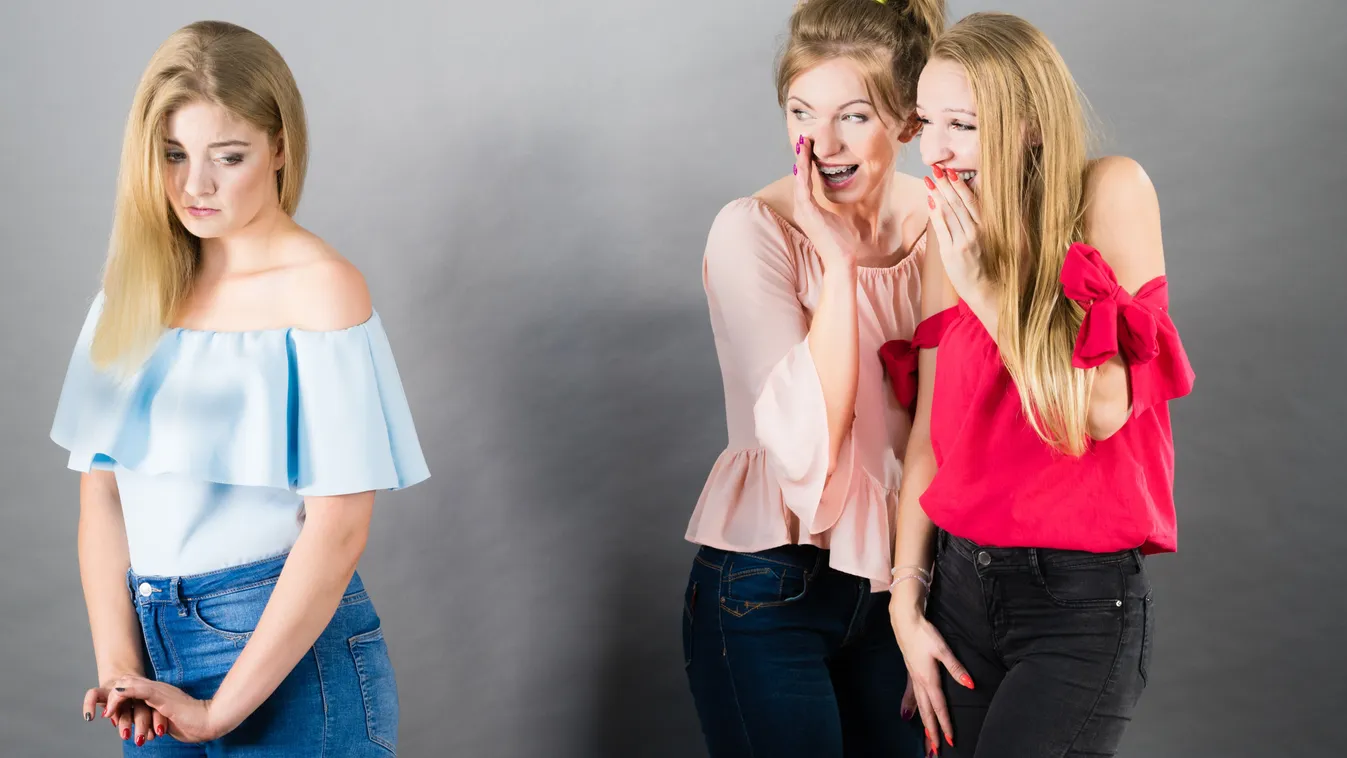 Két barátnő sugdolózása egy skinny farmert viselő lányról