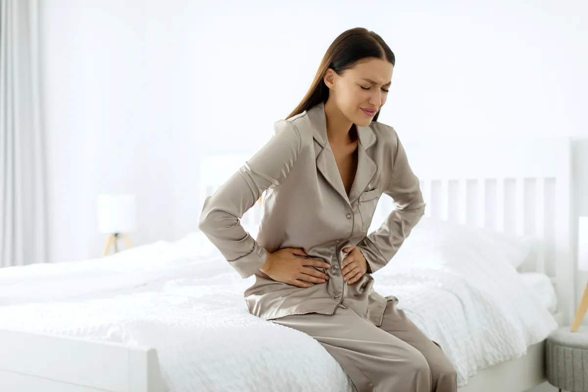 Endometriózissal küzdő fiatal nő az ágyon ülve