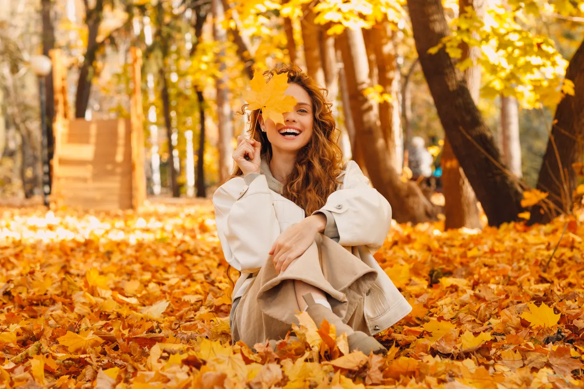 Az őszi falevelek között vidáman ücsörgő fiatal nő