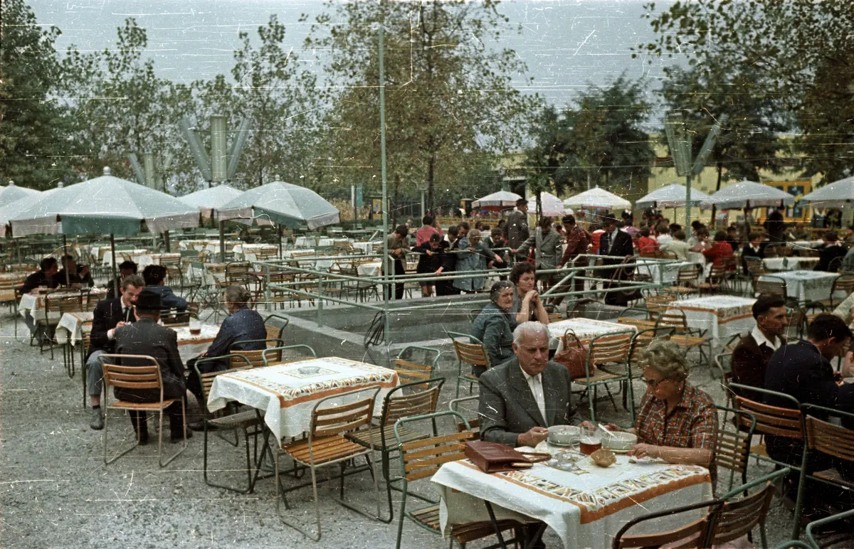 retro fotó egy 50-60 évvel ezelőtti kerthelyiségrő, ahol több ember ebédel.