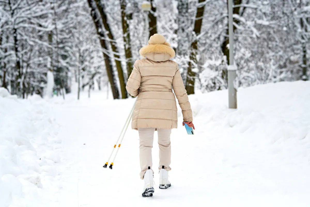 Téli mozgásnak nordic walkingot választó 50 feletti nő a havas tájban