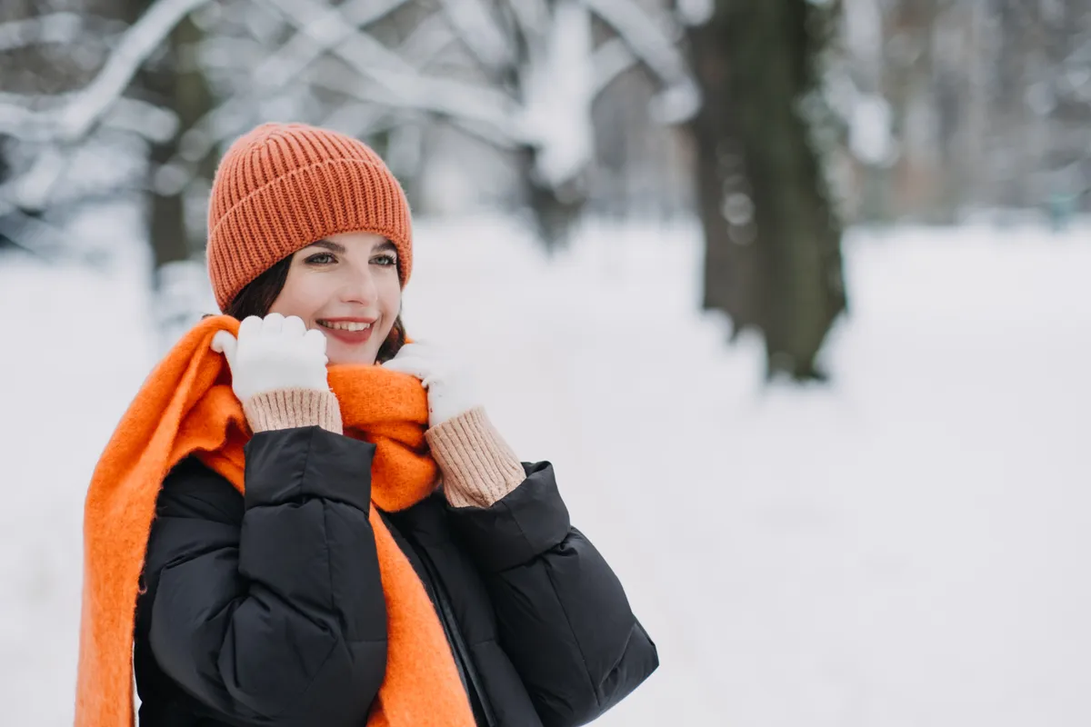 Woman,In,Orange,Winter,Hat,And,Scarf,Smiling,In,Snow-covered